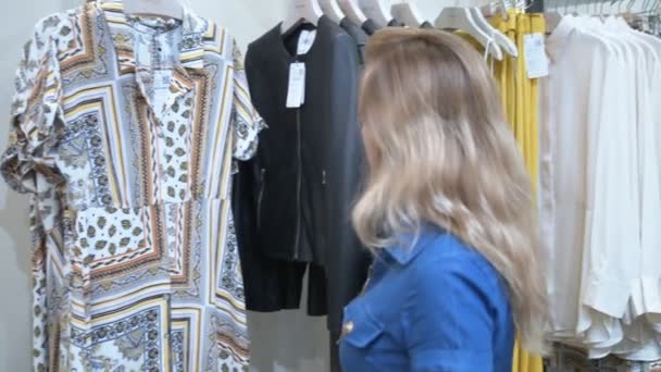 Junge Frau, die in einer Boutique neue Kleider findet. sie liest die Tags und wählt. — Stockvideo