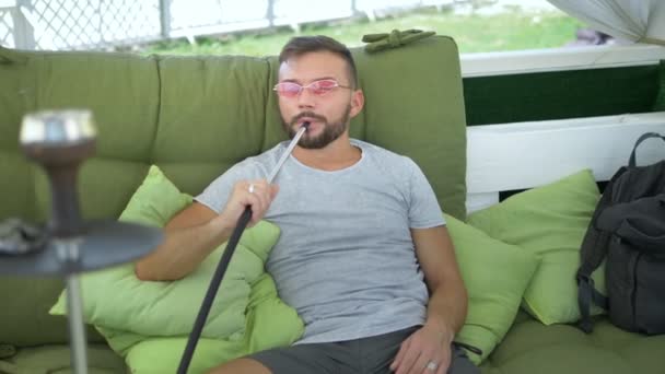 Gancho ao ar livre. homem bonito fuma um narguilé no gazebo em um dia ensolarado de verão — Vídeo de Stock