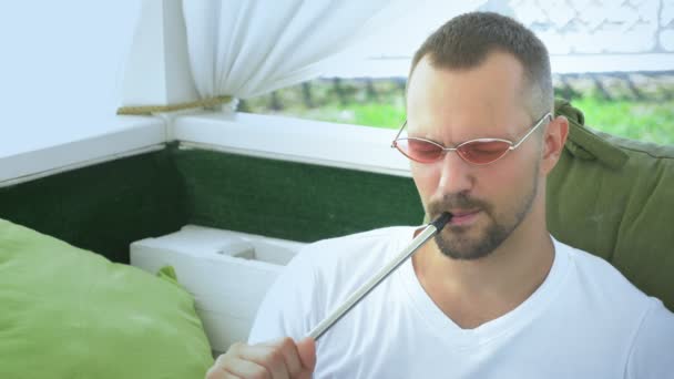 Waterpijp buitenshuis. knappe man rookt een waterpijp in het prieel op een zonnige dag in de zomer — Stockvideo
