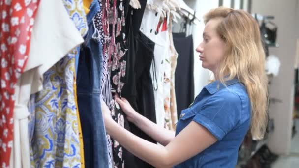 Jeune femme trouver de nouveaux vêtements dans une boutique. Elle lit les étiquettes et choisit . — Video