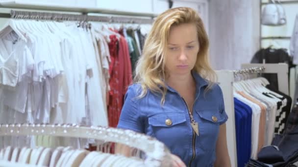 Mujer joven encontrando ropa nueva en una boutique. Lee las etiquetas y elige . — Vídeos de Stock