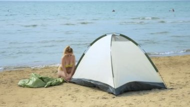 mayo kız yaz aylarında denize karşı kumlu bir plajda kamp için bir çadır koyar