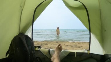 deniz tarafından kamp kavramı. bir adam denize sıçrayan kız arkadaşı için bir çadırdan izler