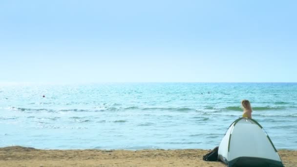 Concept de camping en bord de mer. Fille recueille des coquillages sur la plage près de la tente sur un fond de mer . — Video