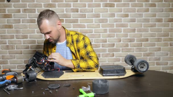 Een mannelijke monteur is het repareren van een elektrische Skate zittend in een workshop in een loft. masterplan — Stockvideo