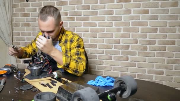 Een mannelijke monteur is het repareren van een elektrische Skate zittend in een workshop in een loft. masterplan — Stockvideo