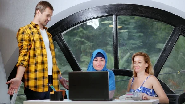 Concept d'équipe multinationale. femme musulmane en hijab, femme caucasienne et homme caucasien travaillant ensemble dans le bureau à l'aide d'un ordinateur portable . — Photo