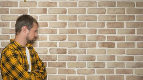 Hombre guapo molesto en una camisa a cuadros de color amarillo a la moda contra una pared de ladrillo, espacio de copia. concepto de gestos y emociones — Foto de Stock