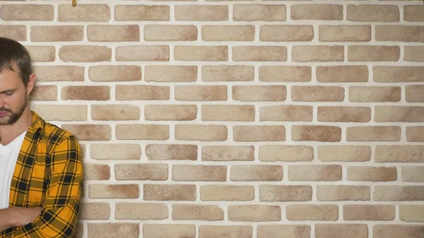 Chateado homem bonito em uma camisa xadrez elegantemente amarelo contra uma parede de tijolo, espaço de cópia. conceito de gestos e emoções — Fotografia de Stock
