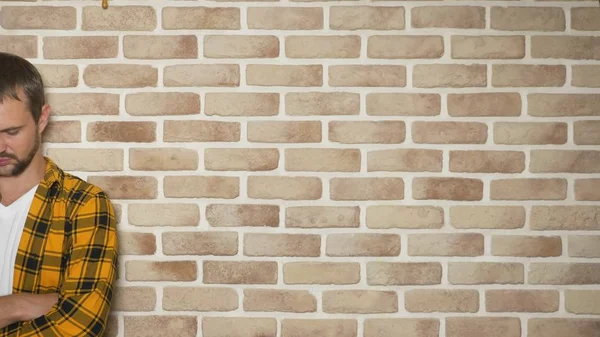 Sconvolto bell'uomo in una camicia a scacchi giallo alla moda contro un muro di mattoni, spazio copia. gesti ed emozioni concetto — Foto Stock