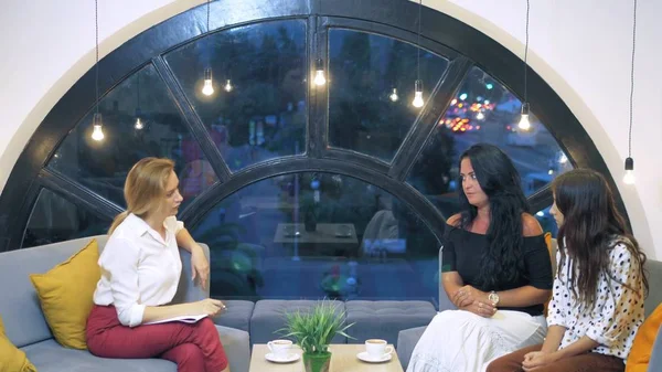 El concepto de salud psicológica en una gran ciudad. Una psicóloga mujer consulta a una mujer y su hija adolescente en una oficina con una gran ventana hermosa desde la que las luces de la ciudad moderna —  Fotos de Stock