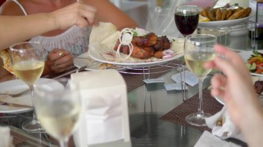 Birisi çatallı bir tabaktan ızgara et alır. Arkadaşlar birlikte yemek yer, sohbet ve içki.