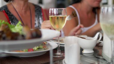 dostça veya aile yemeği. Spot ışıklarında, birisi şişeden bir bardağa şarap döküyor. Insanlar büyük bir masada yiyip içiyorlar.
