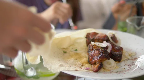 someone takes grilled meat from a plate with a fork. Friends eat food, chat and drink together.