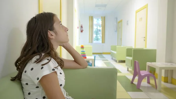 La ragazza è seduta nell'atrio della clinica per bambini, in attesa di un appuntamento con il medico. concetto di visita medica, monitoraggio sanitario, esame preventivo dei medici . — Foto Stock