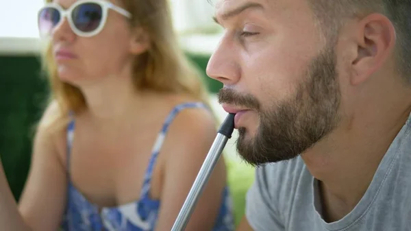 Couple man and woman smoke hookah in the gazebo on a clear sunny day and talk — Stock Photo, Image