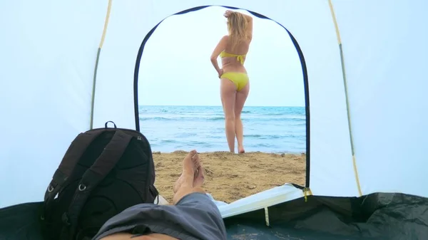 Conceito de acampar junto ao mar. um homem observa de uma tenda para sua namorada que espirra no mar — Fotografia de Stock