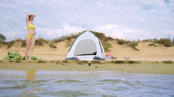 Девушка в купальнике отдыхает рядом с палаткой для кемпинга на песчаном пляже на фоне моря и дюн летом. концепция единства с природой — стоковое фото