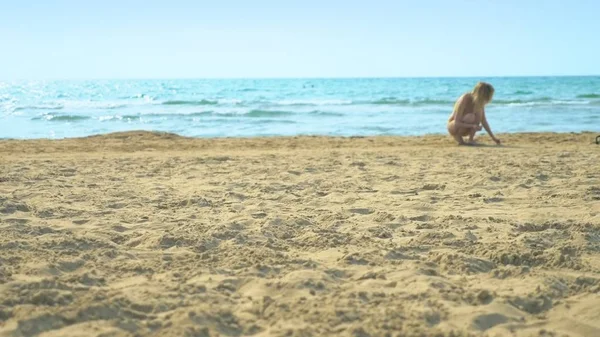 Frau im Badeanzug spaziert am Strand entlang, sammelt Muscheln am Sandstrand. — Stockfoto