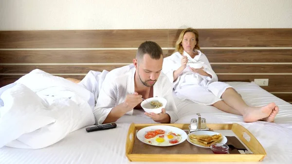 年轻夫妇躺在床上一起在早上，在床上吃早餐 — 图库照片