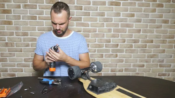 Een mannelijke monteur is het repareren van een elektrische Skate zittend in een workshop in een loft. masterplan — Stockfoto