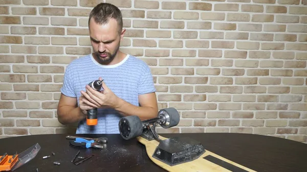 Bir erkek tamirci bir çatı katında bir atölyede oturan bir elektrikli paten tamir ediyor. ana plan
