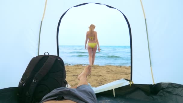 Concetto di campeggio sul mare. un uomo guarda da una tenda per la sua ragazza che schizza in mare — Video Stock