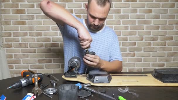 Мужчина-механик чинит электрический скейт, сидящий в мастерской на чердаке. генеральный план — стоковое видео