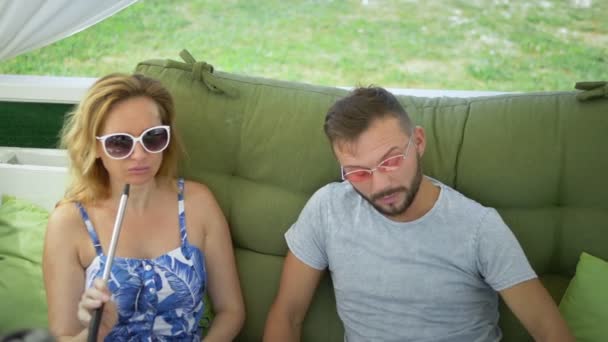 Пара мужчина и женщина курить кальян в беседке в ясный солнечный день и говорить — стоковое видео