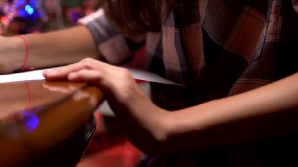 Menina adolescente senta-se em uma mesa perto de uma árvore de Natal decorada e escreve uma carta de Natal para Papai Noel — Vídeo de Stock