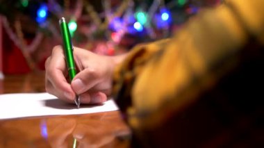 bir adam dekore edilmiş bir Noel ağacının yanında bir masada oturur ve Noel Baba'ya yeni yıl mektubu yazar