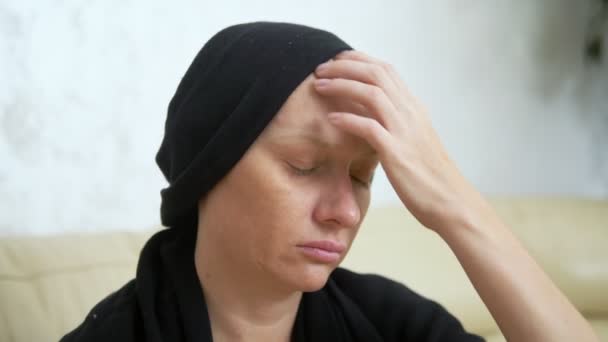 Zieke vrouw in een hoofddoek zittend op een bank. vrouw verwijdert een sjaal uit een kale kop. concept van kankerpatiënten. — Stockvideo
