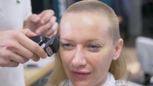 Mulher a rapar a cabeça careca. um cabeleireiro rapa um cabelo longo de mulheres com um cortador de cabelo . — Vídeo de Stock