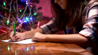 genç kız süslü bir Noel ağacı yakınında bir masada oturur ve Noel Baba bir Noel mektubu yazıyor