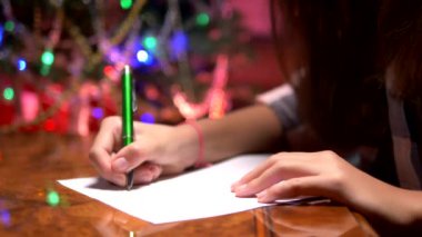 genç kız süslü bir Noel ağacı yakınında bir masada oturur ve Noel Baba bir Noel mektubu yazıyor