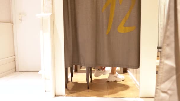 Vrouwelijke benen zijn zichtbaar van onder de gordijnen in de paskamer van een kledingwinkel. — Stockvideo