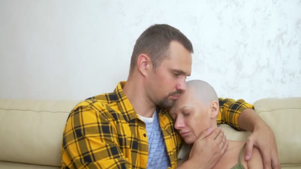 Mujer calva y hombre abrazándose mientras está sentado en un sofá. pareja amorosa superar su oncología juntos — Vídeo de stock