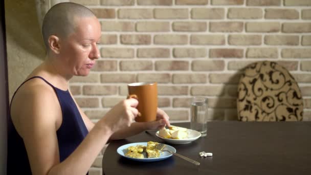 Richtige Ernährung nach Chemotherapie. Eine kahle Frau am Tisch trinkt Pillen beim Essen. — Stockvideo