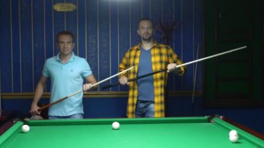 Bilardo masasının yanında dururken iki adam ellerinde bir işaretle dans ediyorlar. Bilardo oynarken arkadaşlarınızla eğlenin.