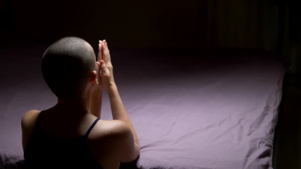 Una donna calva prega in ginocchio vicino al letto. vista posteriore. copia spazio — Video Stock