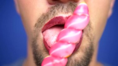 yakın çekim, boyalı dudakları ile sakallı adam bir lolipop yiyor.