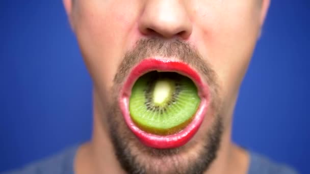 Close-up. grappig beeld van een bebaarde man met lip make-up houden van een kiwi in zijn mond — Stockvideo