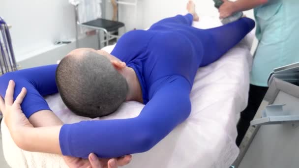 Uma menina careca em um terno roxo recebe um procedimento de massagem lpg . — Vídeo de Stock