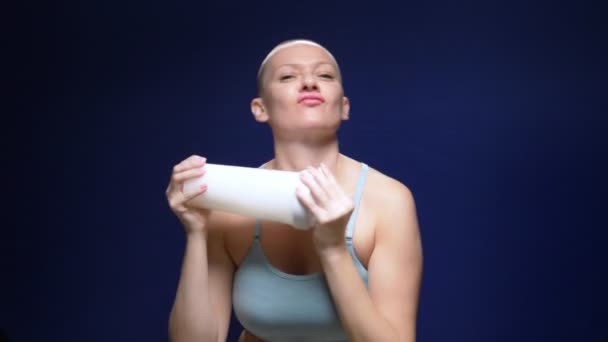 Mulher careca em um top de esportes sacode um coquetel em uma coqueteleira contra um fundo escuro . — Vídeo de Stock