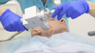 Doktor kozmetik uzmanı, yüzün lazerle yeniden yüzleştirilme prosedürünü uyguluyor. Cilt gençleştirme konsepti, donanım kozmetolojisi.