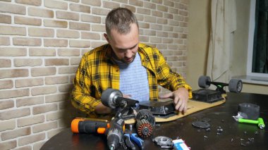 Bir erkek tamirci bir çatı katında bir atölyede oturan bir elektrikli paten tamir ediyor. ana plan