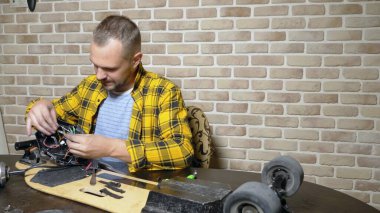 Bir erkek tamirci bir çatı katında bir atölyede oturan bir elektrikli paten tamir ediyor. ana plan