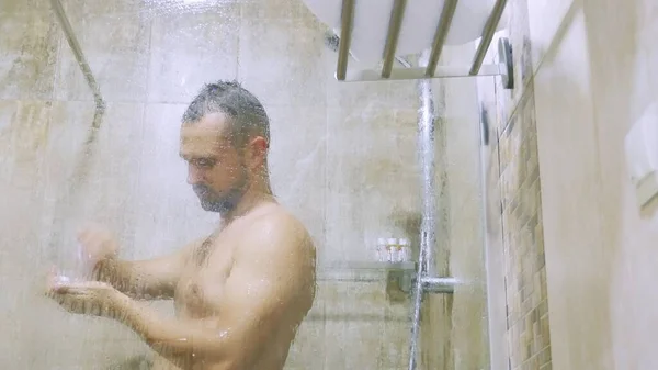 Fiatal jóképű ember érzelmileg énekel, és táncol a zuhany alatt. — Stock Fotó