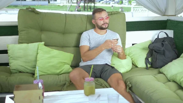 Cara bonito usa um smartphone enquanto relaxa em uma cama gazebo — Fotografia de Stock