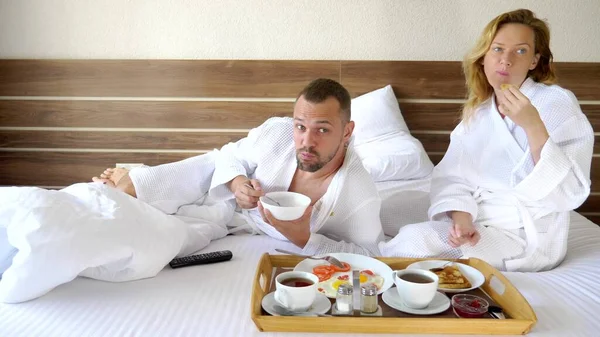 Ungt par som ligger i sängen tillsammans på morgonen, äta frukost på sängen — Stockfoto
